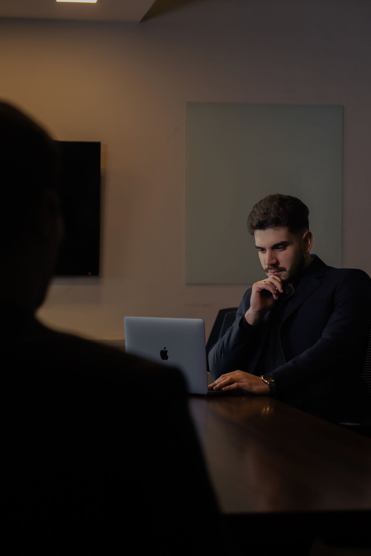 Homem concentrado trabalhando em um notebook Apple em sala de reunião
